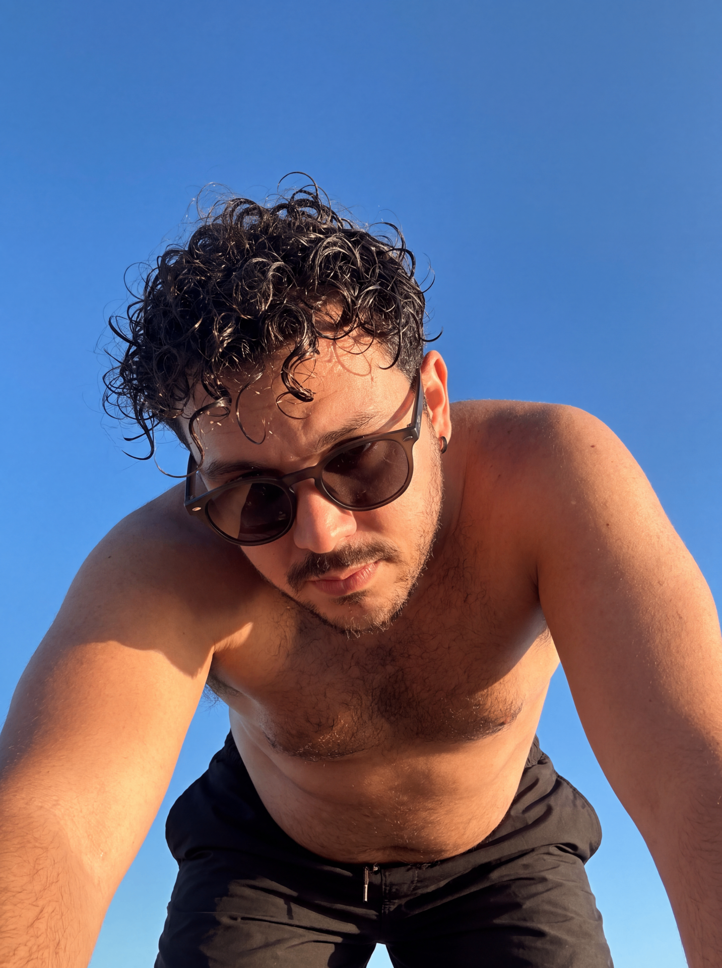 AI-generated character seen from below against a clear blue sky, wearing round sunglasses